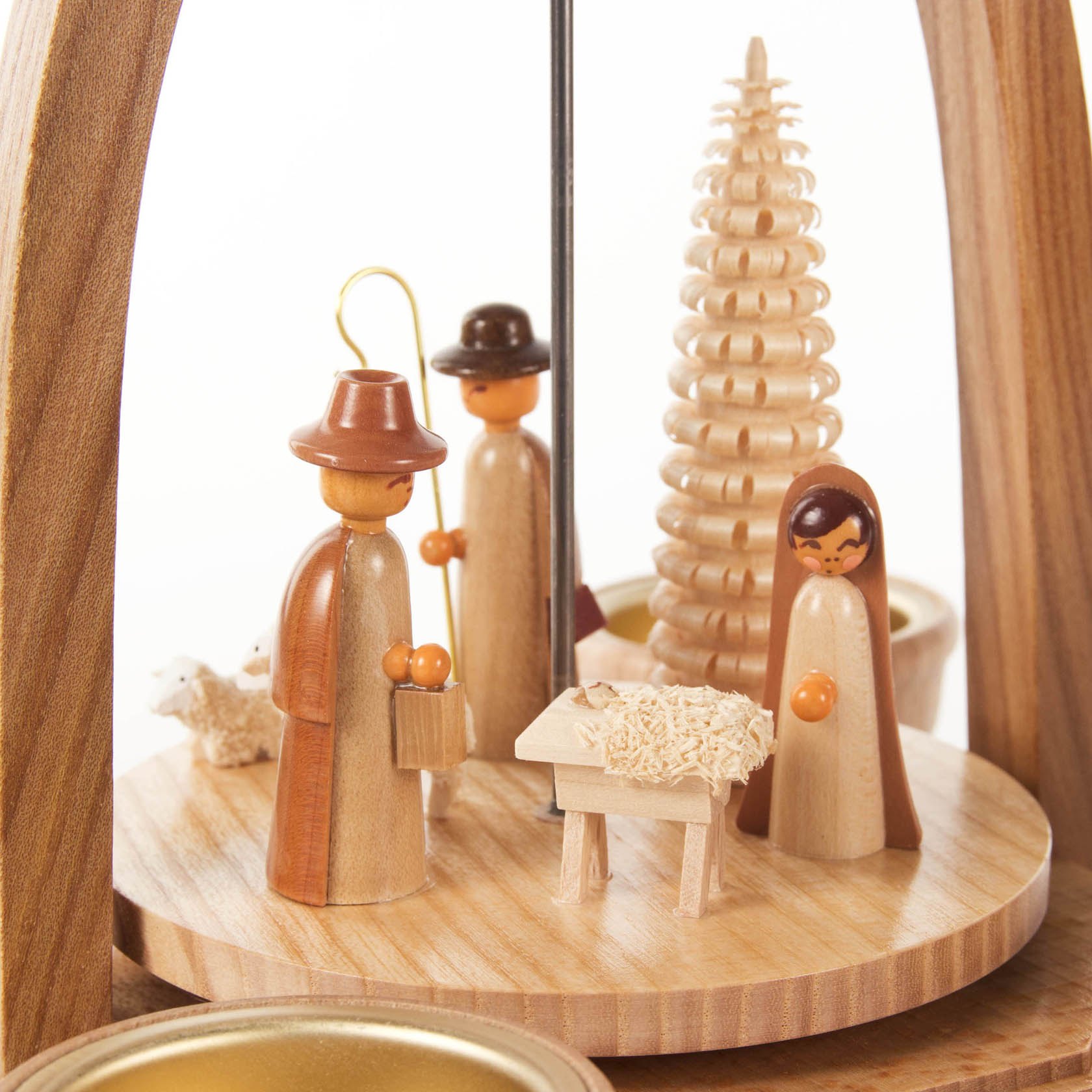 Holzpyramide mit drei Holzfiguren, die Krippenszene mit Maria, Josef und dem Jesuskind darstellt, im Hintergrund ein Baumornament.