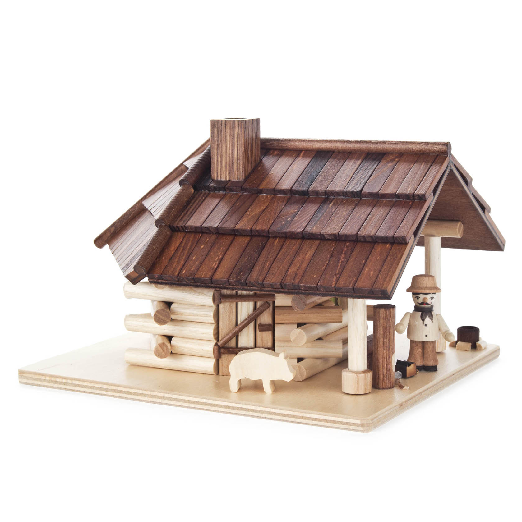 A miniature log cabin with a wooden roof and a small chimney. In front of the cabin stands a wooden figure with a chainsaw, and a small pig figure nearby.