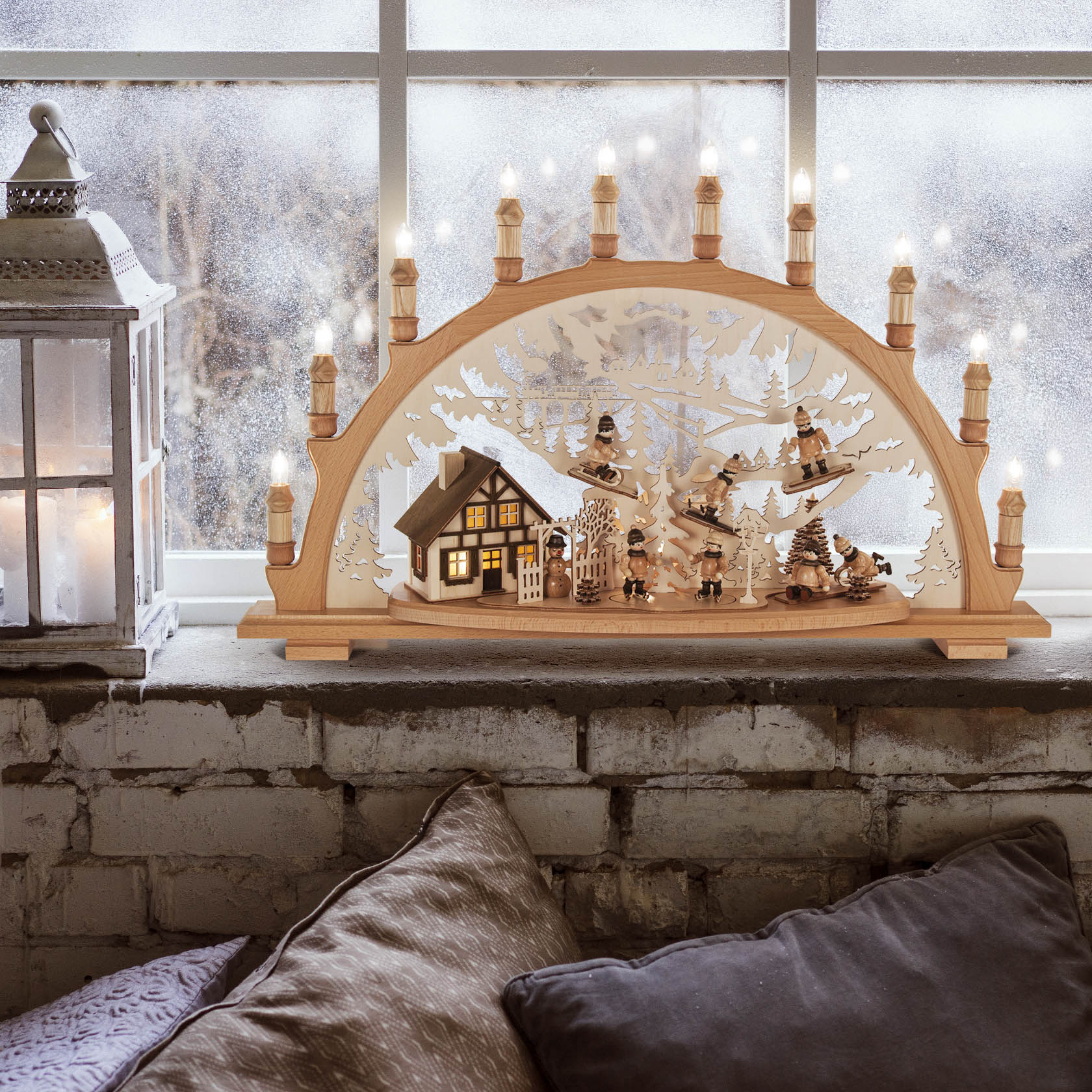 Ein Schwibbogen zeigt ein beleuchtetes Haus und Wintersportler bei Aktivitäten. Hintergrund mit schneebedeckten Bäumen, alles elektrisch beleuchtet.