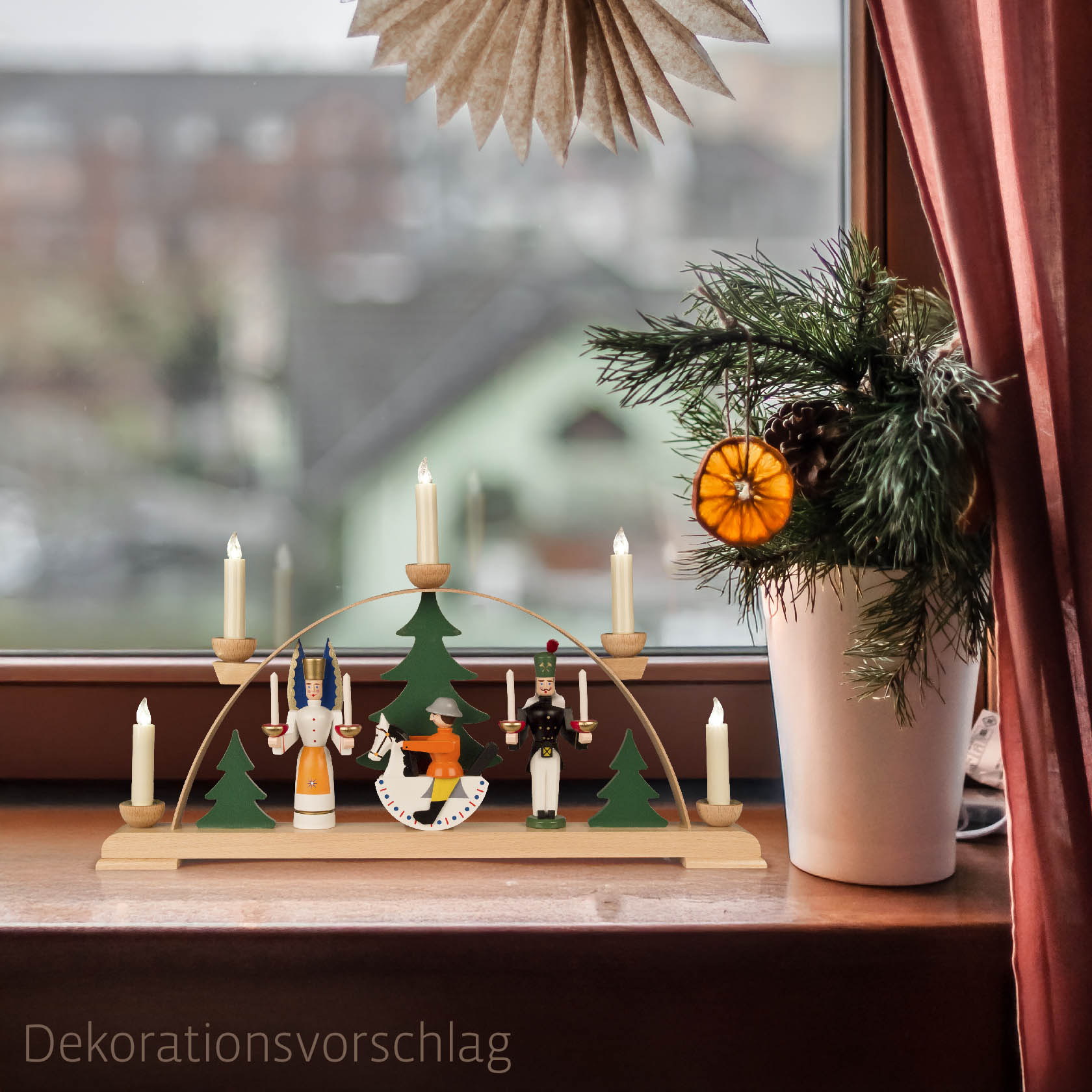 Farbig bemalter Schwibbogen mit Figuren: Engel, Bergmann und Reiterlein, auf Fensterbank platziert. Sechs Kerzenhaltern, Tannenzweige im Hintergrund.