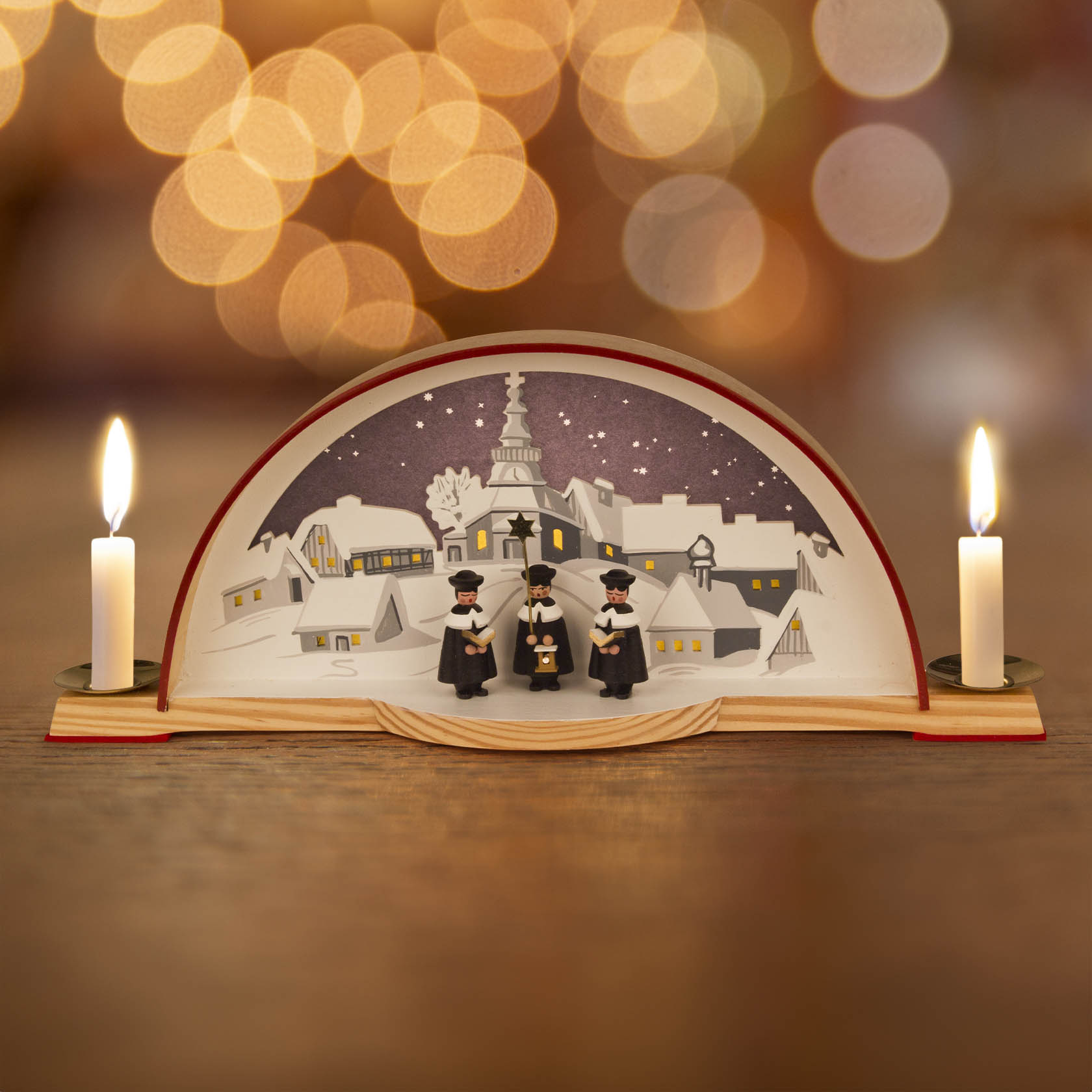 A traditional Schwibbogen arch featuring the Seiffen Church and Kurrende singers, illuminated with electric lighting and two candles on either side.