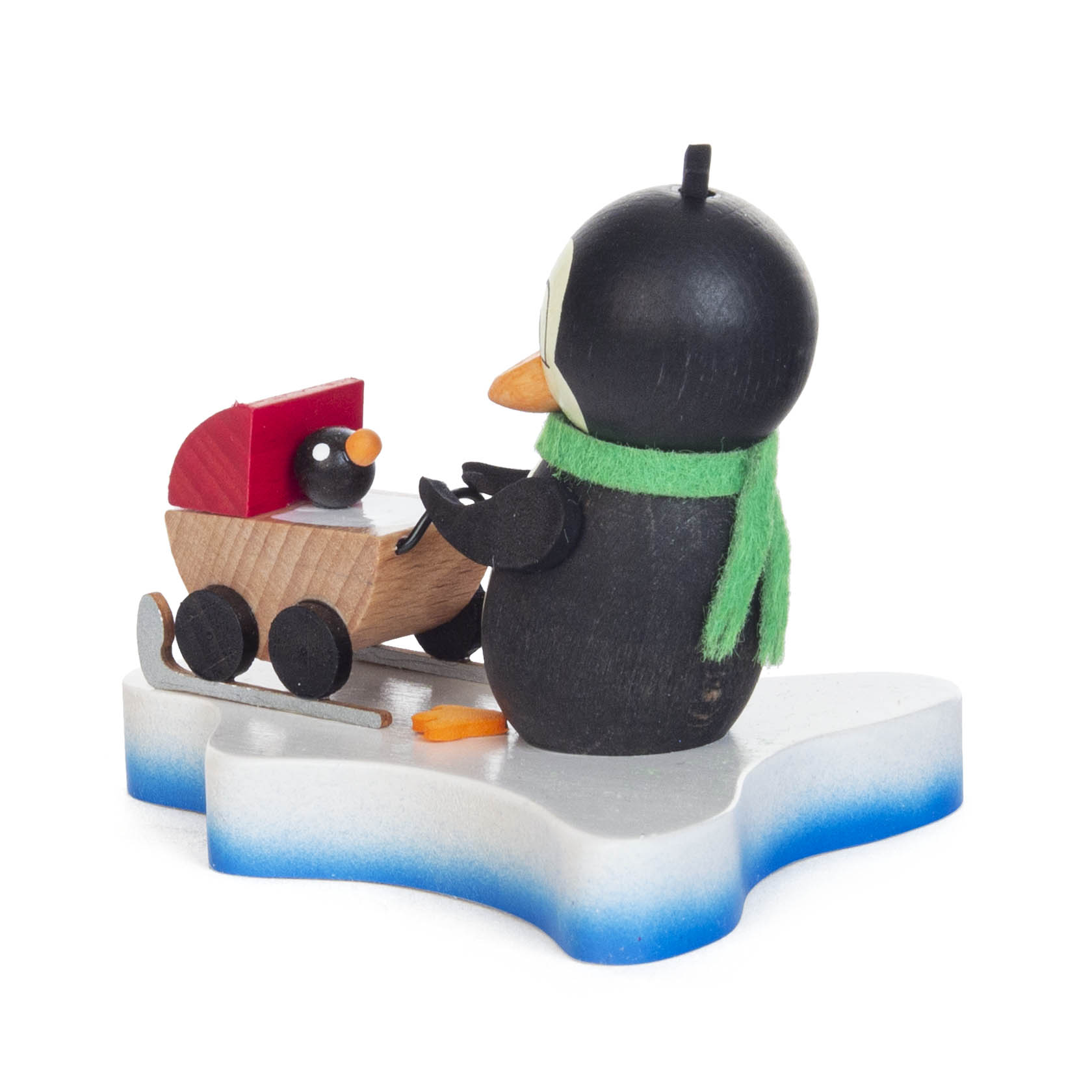 Holzfigur eines Pinguins mit grünem Schal, der einen Kinderwagen mit einem Pinguin-Baby darin auf einem Eissockel schiebt.