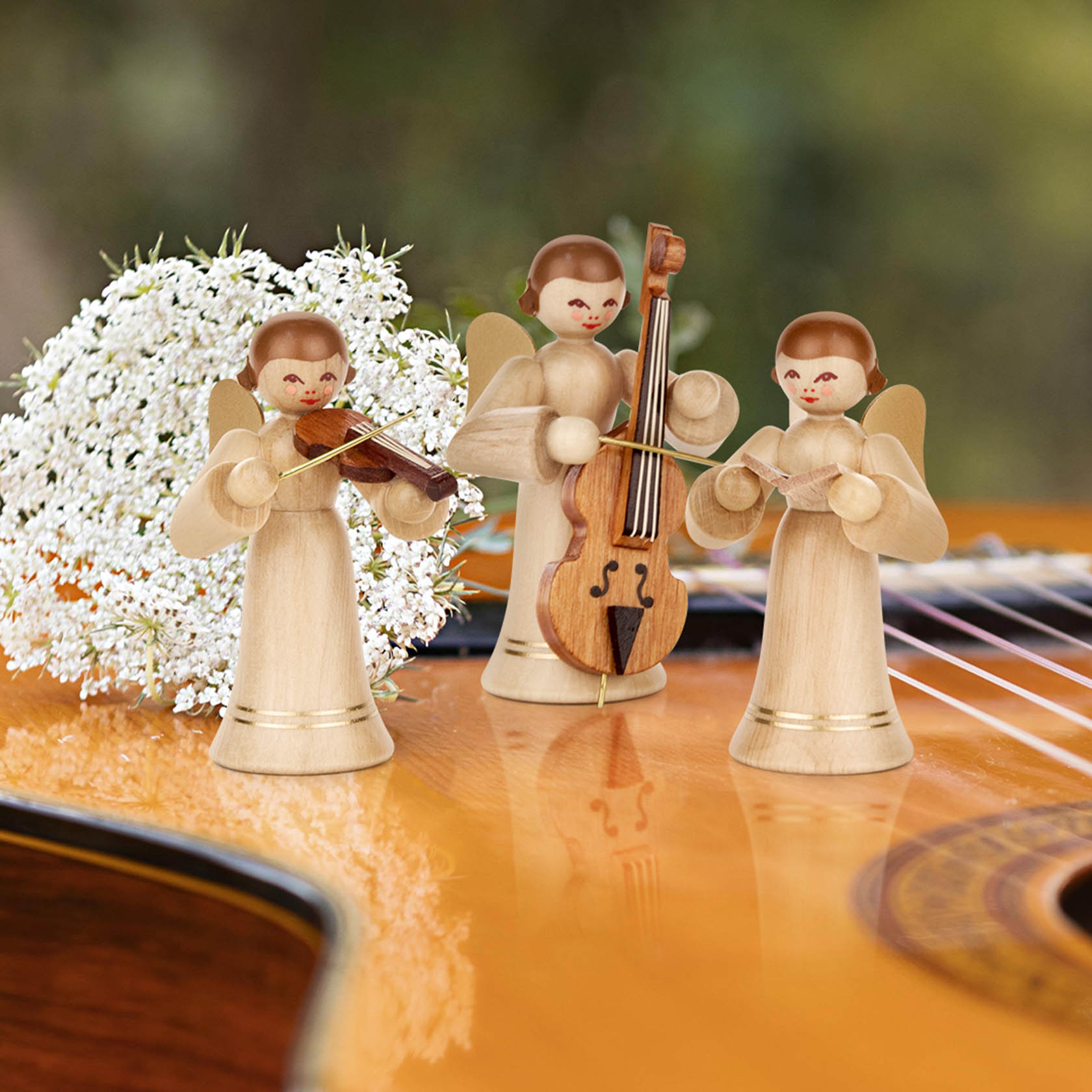 Drei Engelsfiguren aus Holz, mit goldenen Flügeln und langen, naturfarbenen Kleidern, spielen Geige, Cello und Flöte auf einer Gitarre.