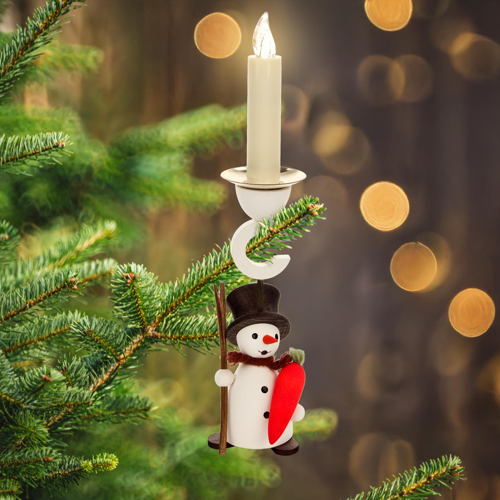 A decorative snowman candle holder designed to hang. The snowman, wearing a black hat, is holding a large red carrot. A 14mm candle is placed above it.