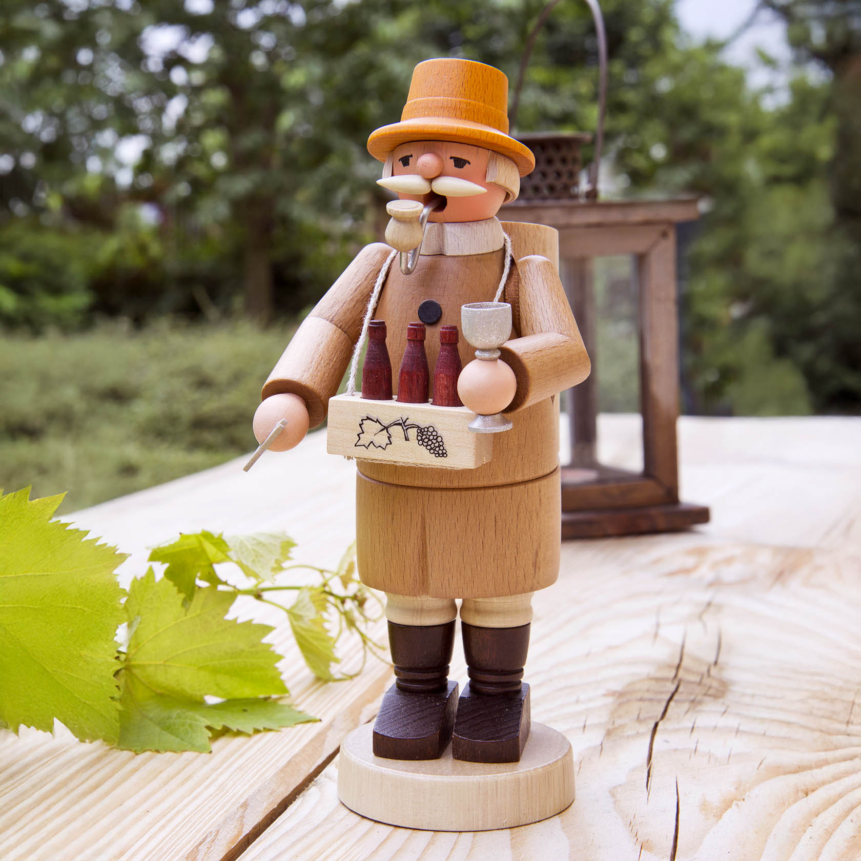 Wooden incense smoker figure depicting a winemaker holding a wine glass and a tray with wine bottles, standing on a wooden surface with a grapevine leaf.