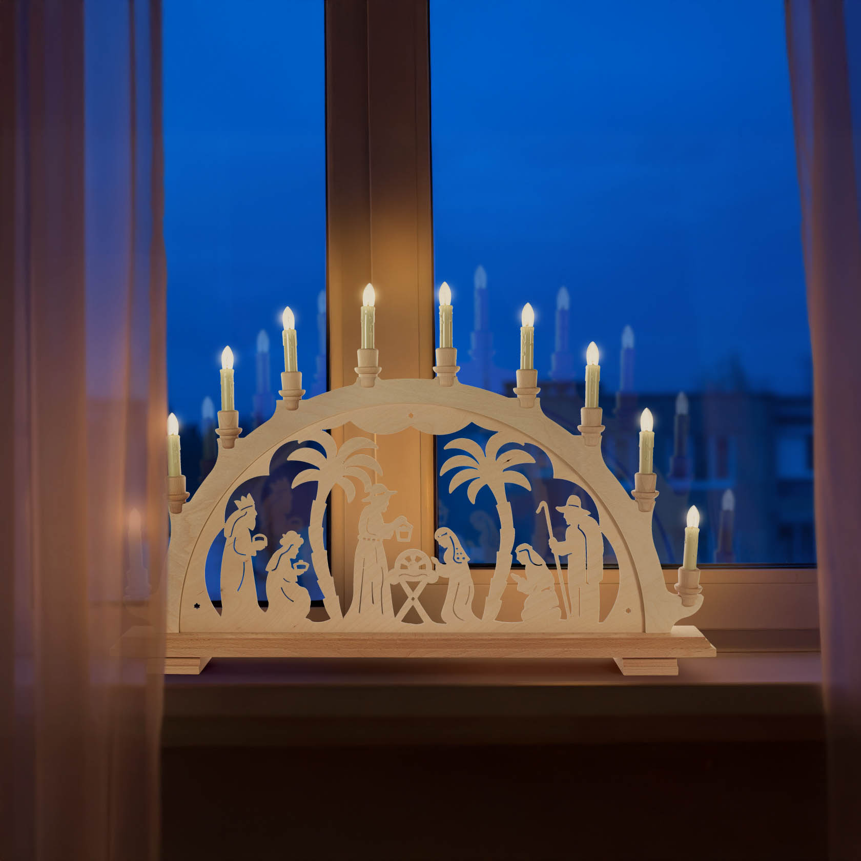 Ein beleuchteter Schwibbogen aus Holz zeigt die Szene der Geburt Christi mit Figuren von Maria, Josef, dem Jesuskind in der Krippe, den drei Weisen und Palmen.