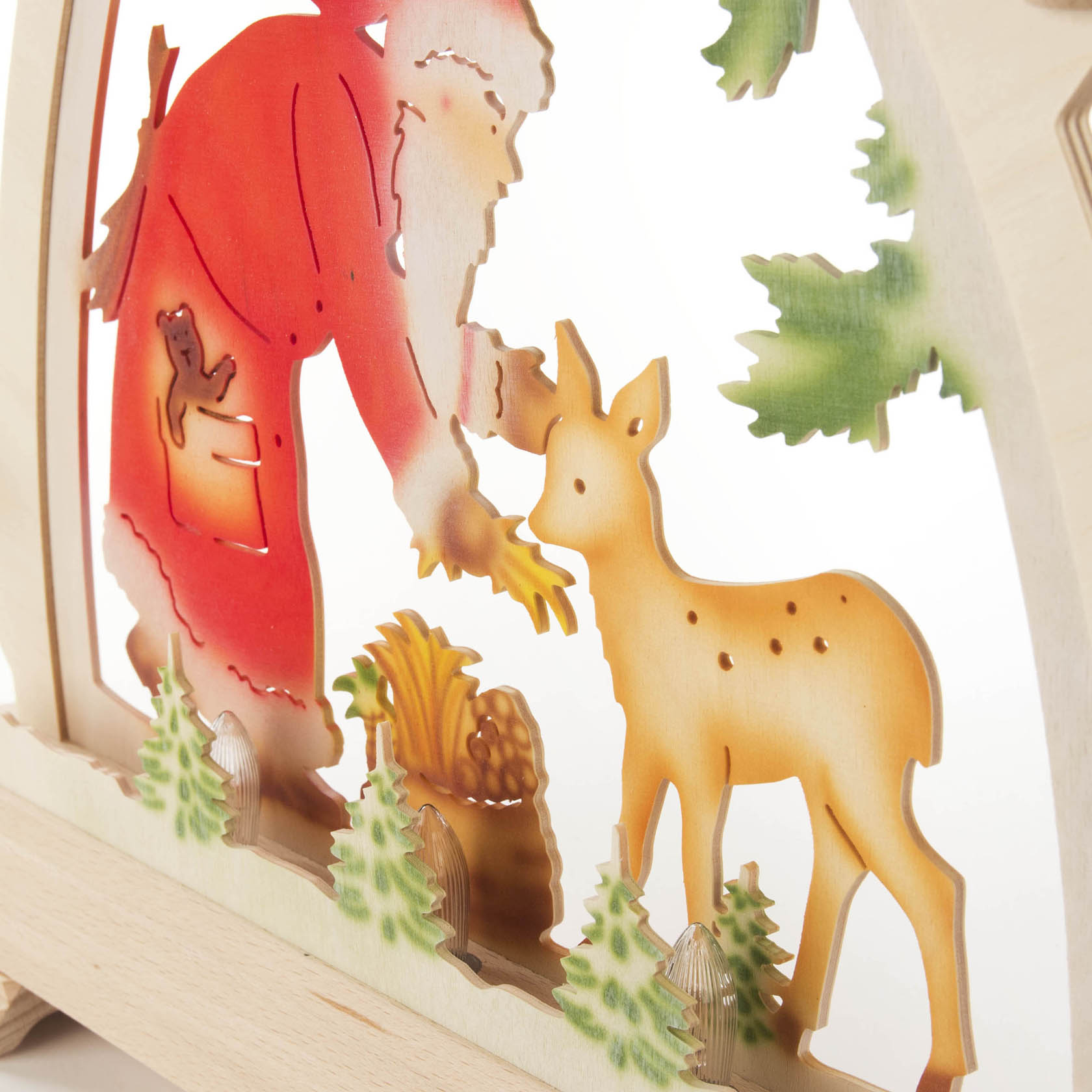 Holzleuchter zeigt Weihnachtsmann in rotem Gewand mit Geschenkesack, der einem Reh Karotten anbietet. Beleuchtet von kleinen weißen Lichtern.