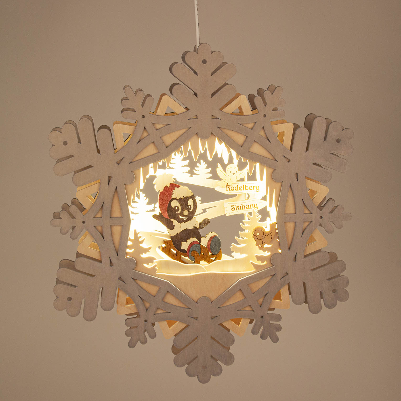 Illuminated window decoration featuring a colorful Pitti character and forest animals, with a snowflake-shaped wooden frame and electric lighting.