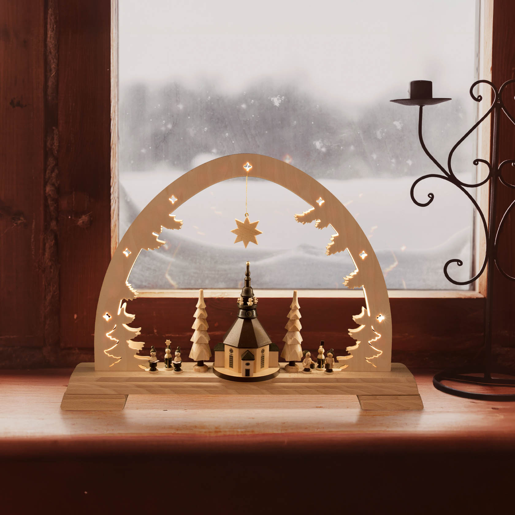 Wooden arch with LED lights featuring the Seiffen Church, flanked by illuminated trees and figurines, set on a wooden base by a window.