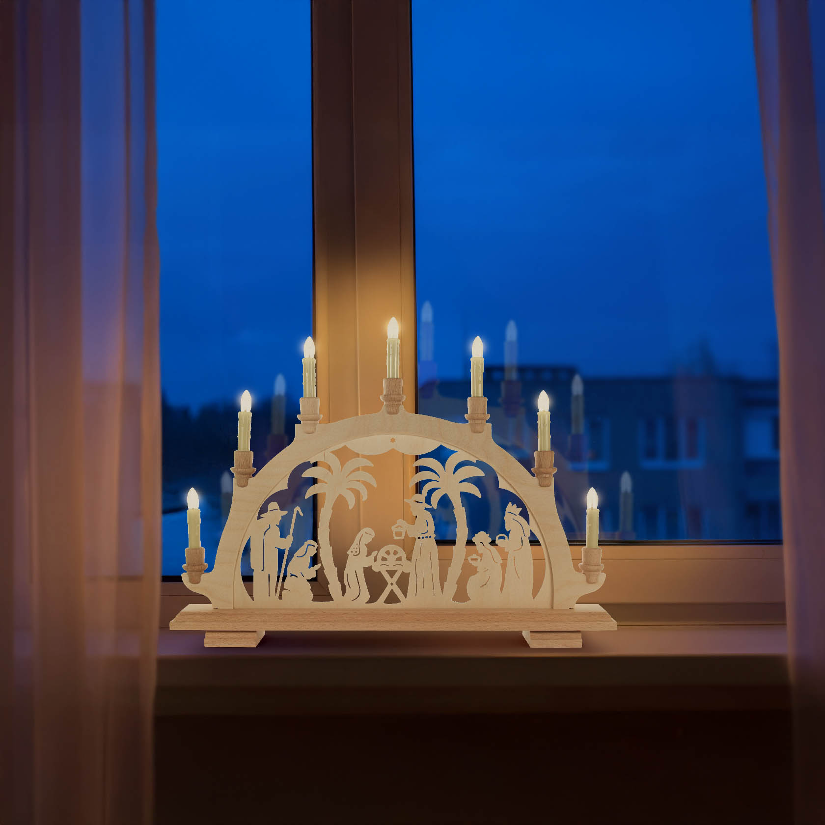 An illuminated electric Schwibbogen featuring a carved scene of the Nativity, showcased on a window sill with candles glowing.