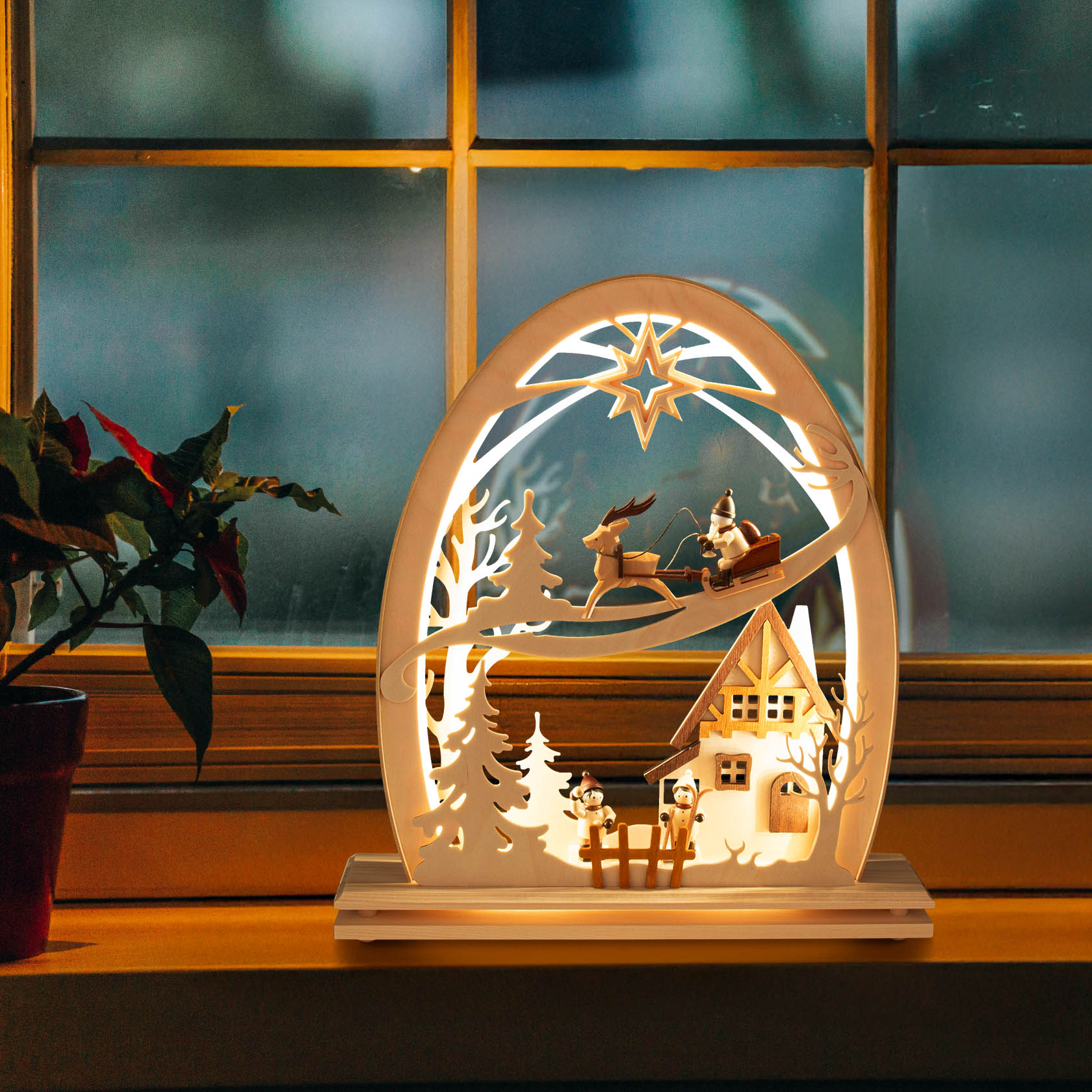 Wooden arch with LED lights depicting a Christmas scene, showing Santa in a sleigh pulled by reindeer above a house with trees.