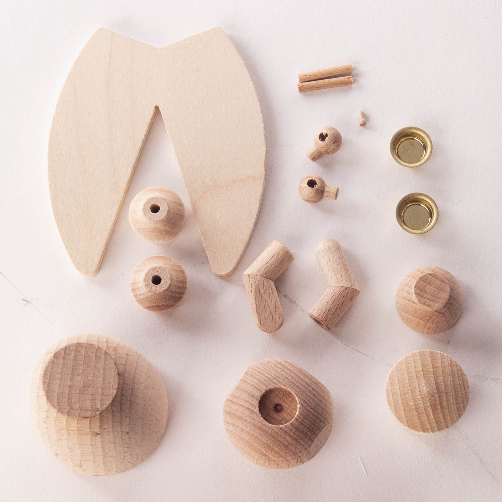 A DIY angel set with wooden parts, including a large wing piece, spherical body parts, circular bases, two small gold cups, and pegs.