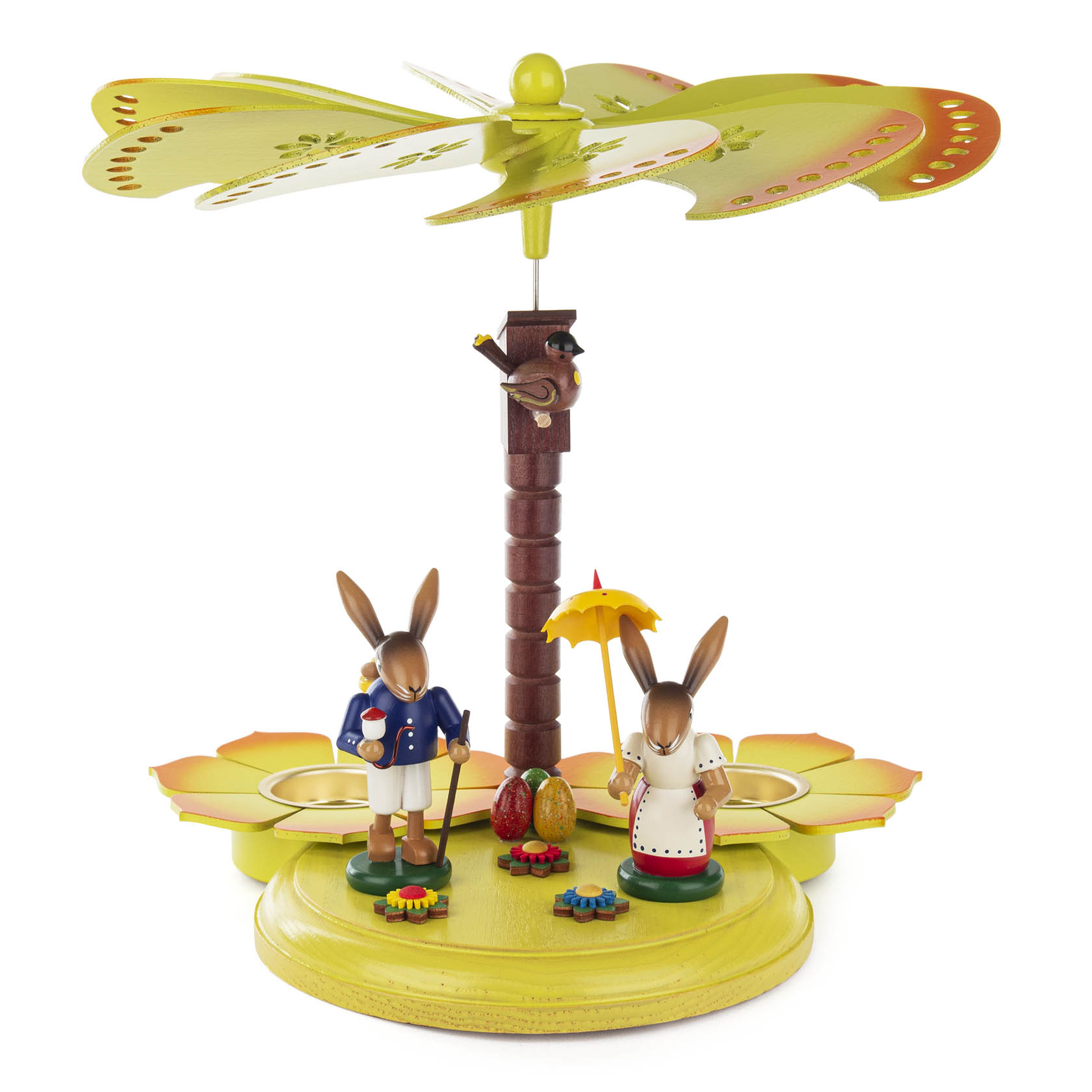Teelichtpyramide mit zwei Hasenfiguren, einer mit blauer Jacke und Kiepe, der andere mit gelbem Regenschirm, bunte Eier und Blumen auf grünem Sockel.