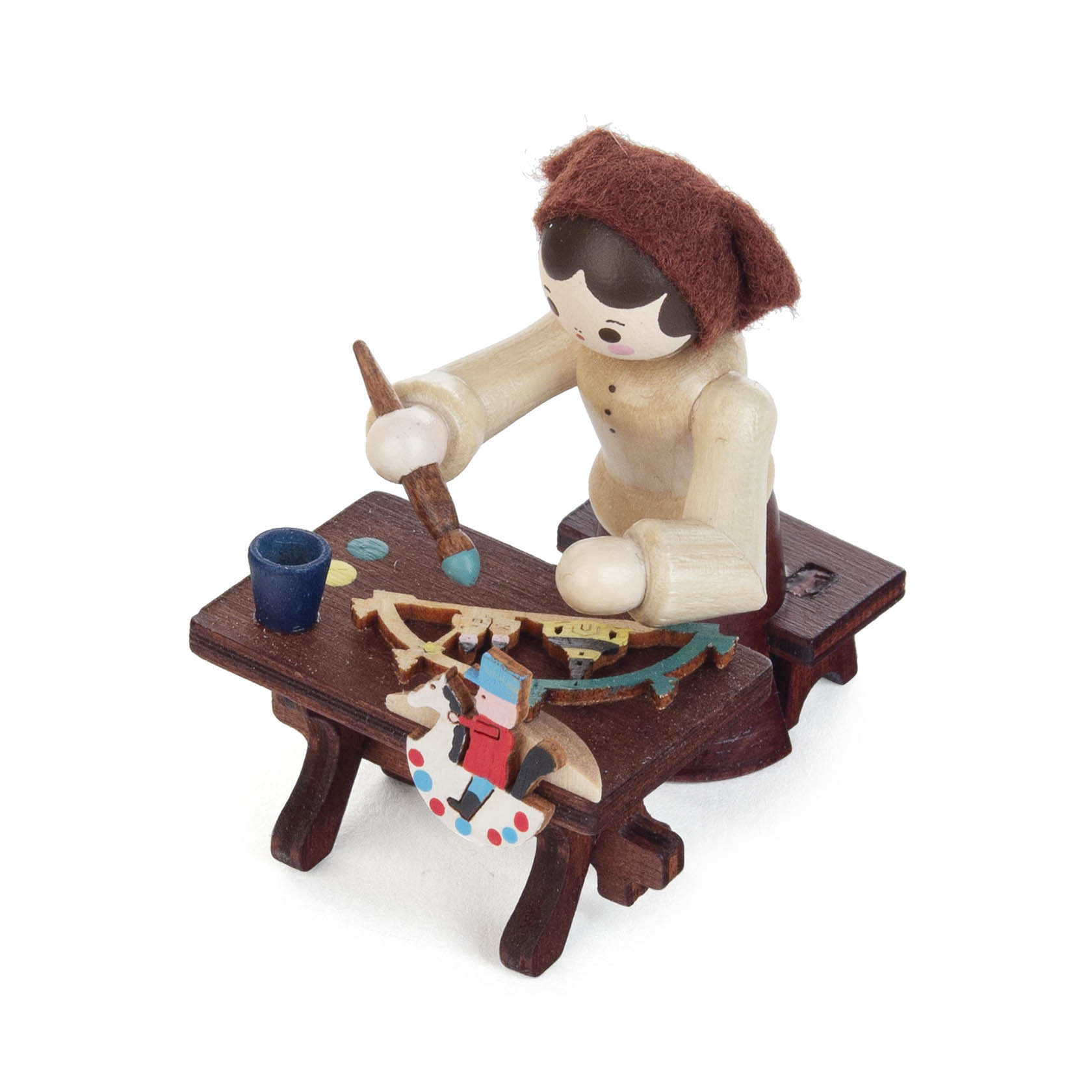 A wooden figurine of a female candle arch painter, dressed in natural colors, seated at a small brown table, painting a Schwibbogen with a brush.