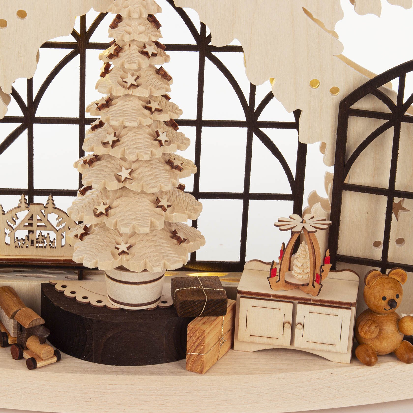 A detailed wooden Christmas arch featuring a carved fir tree, miniature presents, a cabinet with candles, and a teddy bear.