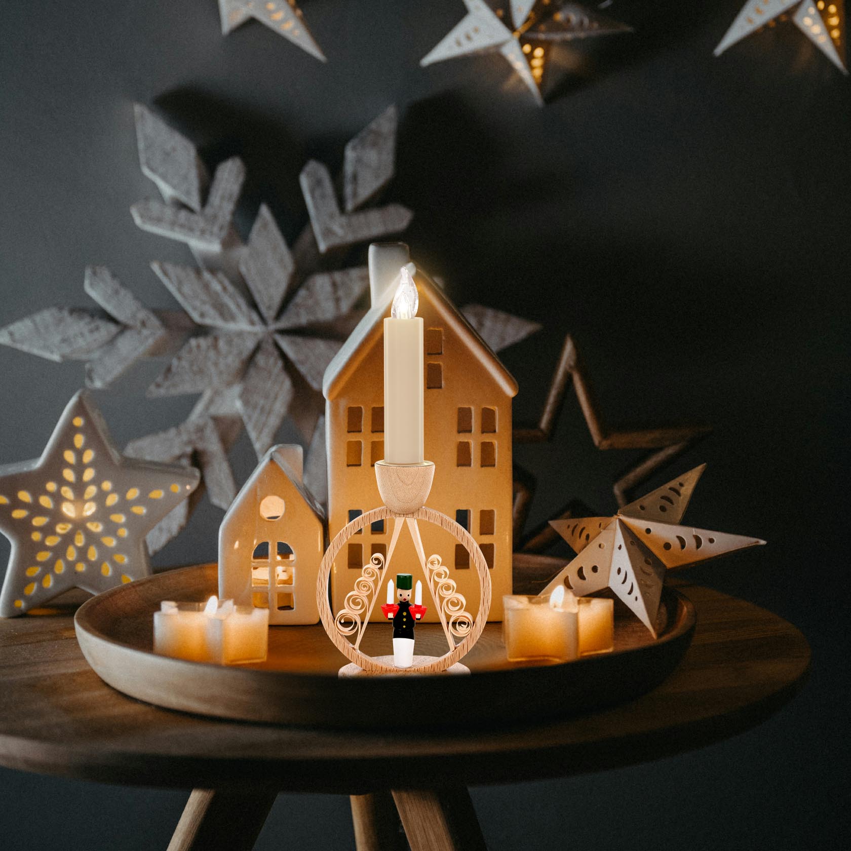 A wooden miner candle holder shaped in a circular design, holding a lit white candle, surrounded by small houses and decorative stars.