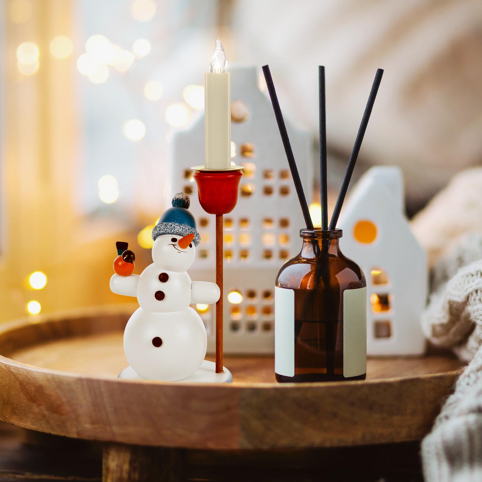A snowman figurine with a blue bobble hat holding a candle holder for a 14mm candle, standing on a wooden surface next to a dark glass bottle with sticks.